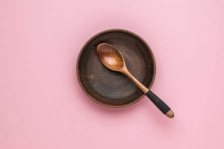 A set of a wooden spoon and a clay bowl on a pink background. Vintage tableware. Flat lay.の写真素材