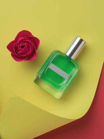 A bottle of perfume and a bright red rose on an abstract yellow and red background. The concept of...