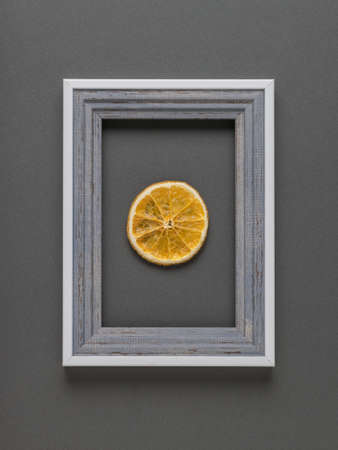 A piece of dried orange in a gray frame on a gray background. Contemporary art. Creative image.の写真素材