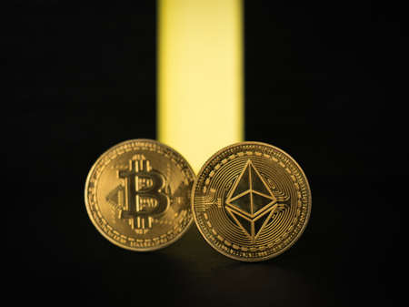 Two popular digital coins and a yellow ray on a black background. The concept of the rise in the price of cryptocurrency. Digital currency.の写真素材