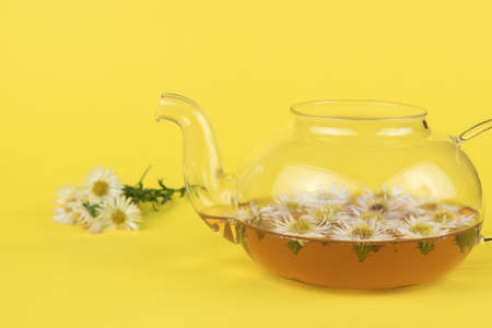 A glass teapot with floral tea and a bouquet of flowers on a yellow background. Medicinal tea.の写真素材