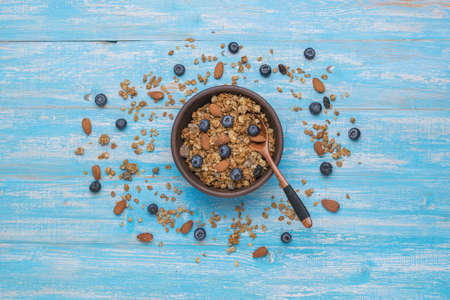 A clay bowl filled with muesli with nuts and blueberries on a wooden table. Healthy vegetarian breakfast. Flat lay.の写真素材