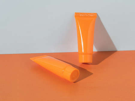 Two orange closed tubes on a white and orange background. Cosmetic creams.の写真素材