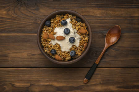Wooden spoon and bowl with muesli and yogurt on a wooden table. Healthy vegetarian breakfast. Flat...