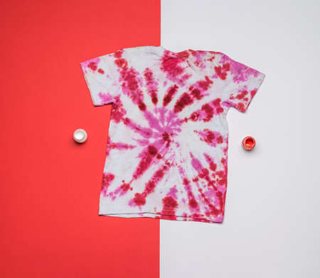 Red and white tie dye T-shirt and paint on a red and white background. Coloring clothes by hand at home. Flat lay.の写真素材