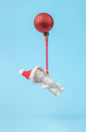 A figurine of a baby in a red cap flying on a Christmas ball. Minimalism. The concept of the new year.の写真素材