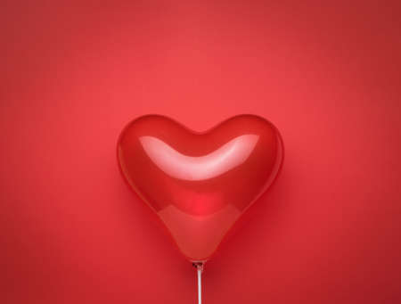 A balloon in the form of a bright red heart on a bright red background. Space for text. The concept of Valentine's Day.の写真素材