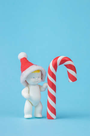 A figure of a baby in a red cap standing next to a red and white candy. Minimalism. The concept of the new year.の写真素材
