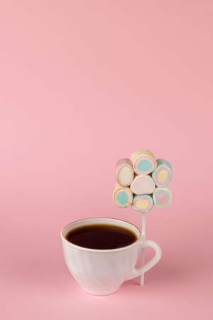 Black coffee in a white cup and a set of marshmallows on a stick on a pink background. The concept of a fun breakfast. Happy morning. Place for text.の写真素材