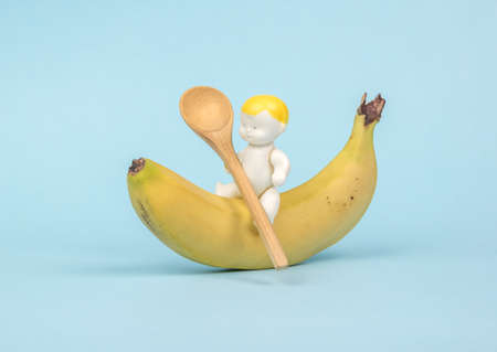 A figurine of a baby sitting on a banana with a wooden spoon. Banana dessert. The concept of healthy baby food.の写真素材