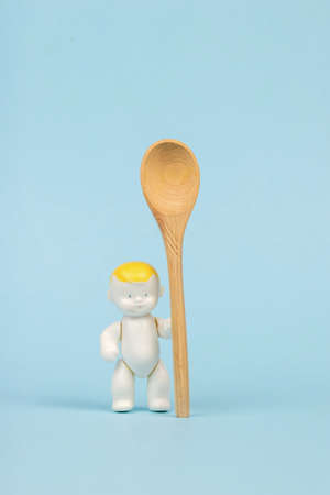 A baby figurine with a large wooden spoon on a blue background. The concept of children's healthy nutrition.の写真素材