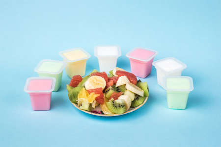 A bowl with sliced fruit and cups with multicolored yogurt on a blue background. Milk and fruit food.の写真素材