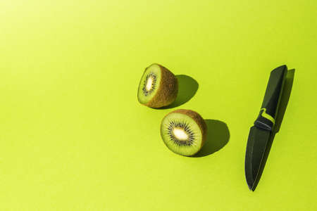 A knife and a cut fruit of a ripe kiwi on a green background. Tropical fruits.の写真素材