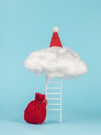 A staircase with a cloud, a large red bag with gifts and a red cap on a blue background. The concept of surprises from Santa Claus.の写真素材