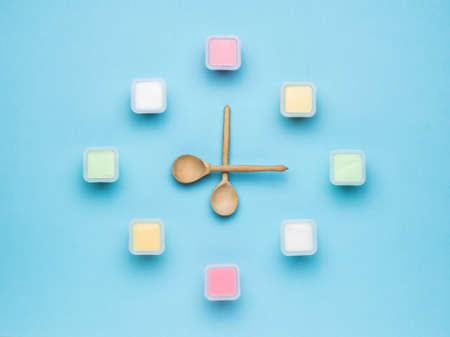 A clock made of plastic cups with yogurt and wooden spoon-shaped hands. The concept of healthy eating. Fruit and milkshakes. Flat lay.の写真素材