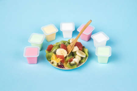 A wooden spoon in a bowl with fruit salad and cups with multicolored yogurt. Milk and fruit food.の写真素材