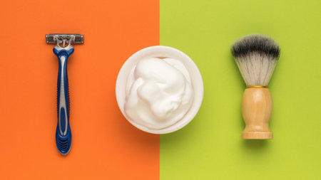 A brush, a plastic razor and a bowl with foam on an orange and green background. Men's accessories for appearance care. Flat lay.の写真素材