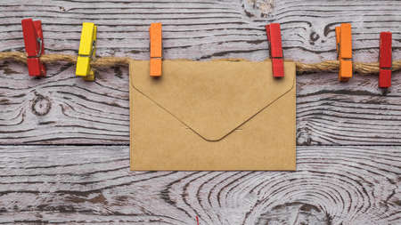 Multicolored clothespins and a postal envelope on a rope on a wooden background. The concept of...