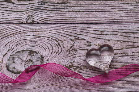 Bright ribbon and transparent glass heart on a wooden background. The concept of Valentine's Day....