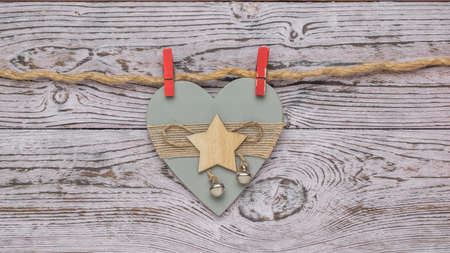 Two red clothespins hold a wooden decoration in the form of a wooden heart on a wooden background. The concept of Valentine's Day.の写真素材