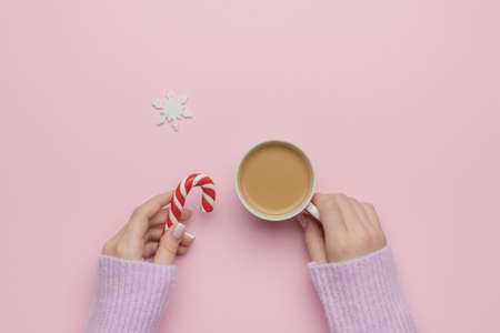 Women's hands with a cup of coffee and sweets on a pink background with a snowflake. The concept of drinking a popular drink. Flat lay.の写真素材