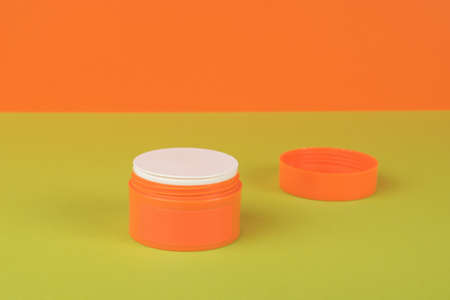 An open orange jar with cream on a green and orange background. A skin care product.の写真素材