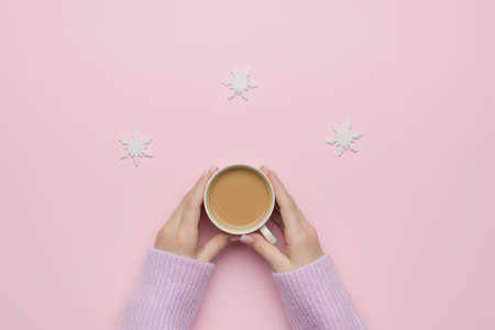 Hands of a girl with a cup of coffee with cream on a pastel background with snowflakes. The concept of drinking a popular drink. Flat lay.の写真素材