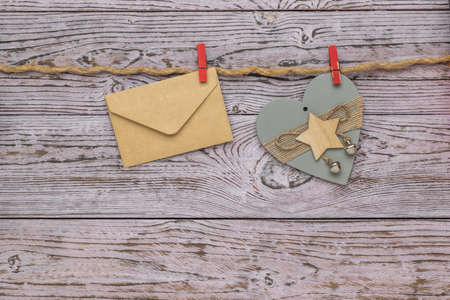 Postal envelope and decoration in the form of a wooden heart on a rope on a wooden background. The concept of Valentine's Day. Flat lay.の写真素材