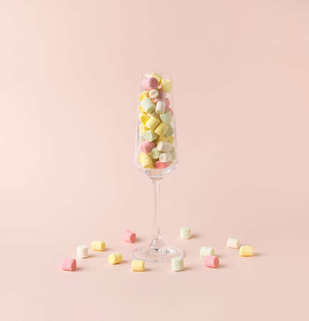 A tall glass glass with pieces of multicolored marshmallows on a beige background. The concept of happiness and success.の写真素材
