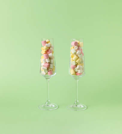 Two tall glass glasses filled with colorful marshmallows on a green background. The concept of happiness and success.の写真素材