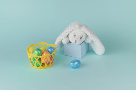 A basket with colorful Easter eggs and a bunny peeking out of a gift box. The concept of Easter.