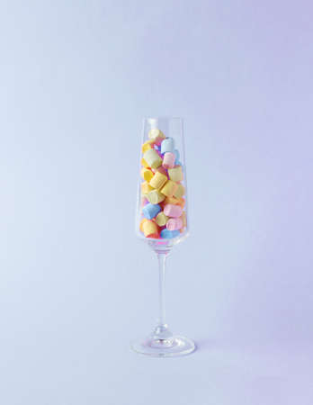 A tall glass glass with multicolored marshmallows on a purple background. The concept of parties. The concept of happiness and success.の写真素材