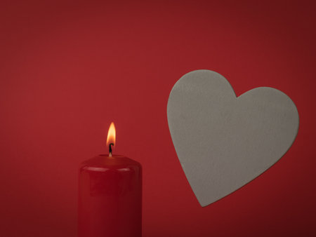 A burning candle on a red background and a large gray wooden heart. The concept of a romantic relationship.の写真素材
