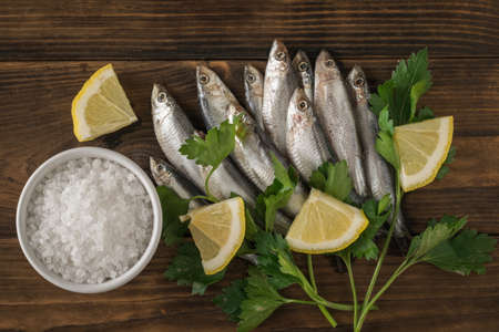 A bowl with coarse sea salt and sprat with herbs and lemon on a wooden table. Delicious seafood...