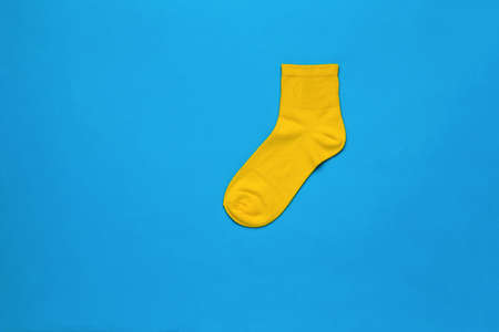 Bright yellow sports sock on a blue background. A stylish sports accessory. flat lay.