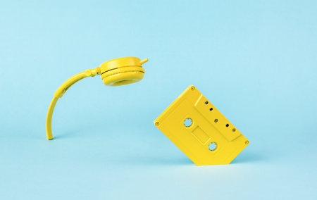 Yellow headphones and a tape recorder sticking out of the blue background. Vintage style in sound recording. flat lay. Minimal audio concept.の写真素材