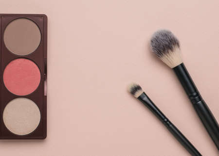 Pastel-colored face shadows and two makeup brushes on a beige background. Popular modern cosmetics. flat lay.の写真素材