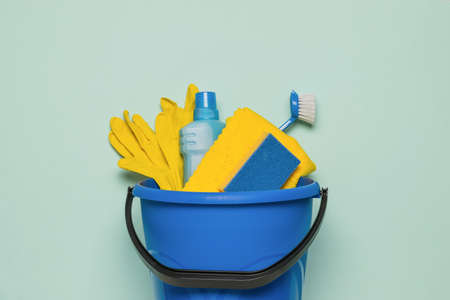 A blue bucket with a set of cleaning tools on a light background. The concept of cleaning the...