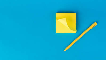 A stack of yellow note paper and a yellow pen on a blue background. Stylish stationery.の写真素材