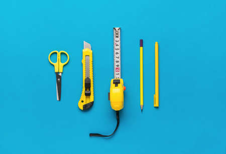 Measuring tape, scissors, knife, pen and pencil on a blue background. A set for creativity of yellow...