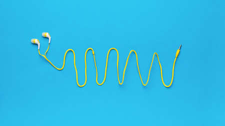 Headphones for a smartphone with a long yellow wire on a blue background. minimal concept. flat lay.の写真素材