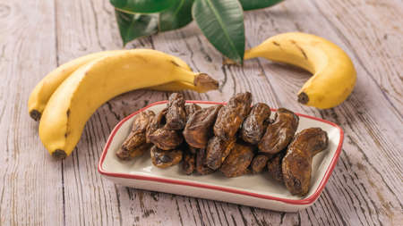 Fresh bananas and a bowl of dried bananas on a wooden table. Delicious natural fruit snack.の写真素材