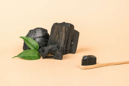 A toothbrush with charcoal toothpaste and pieces of charcoal on a beige background. Teeth whitening and dental care products.の写真素材