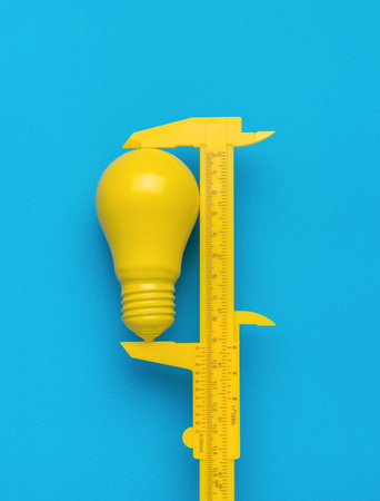 The minimal concept of the idea. A yellow caliper measuring a yellow light bulb on a blue...