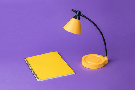 A table lamp with a yellow notebook on a purple background. desktop lighting.の写真素材