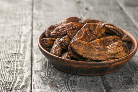 Dried bananas in a clay bowl on a black wooden table. Delicious natural fruit snack.の写真素材