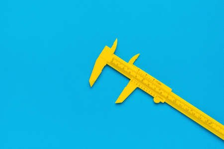 A yellow plastic caliper on a blue background. A tool for accurate measurement of dimensions.の写真素材