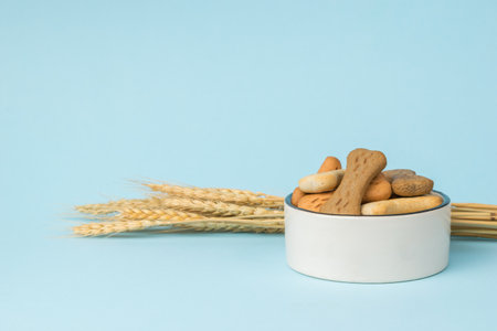 A bowl of cookies for dogs and ripe ears of corn on a blue background. A delicious treat for dogs with cereals.の写真素材