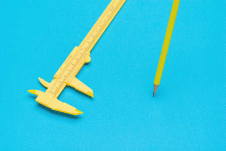 Yellow pencil and caliper on a blue background. A tool for accurate measurement of dimensions.の写真素材