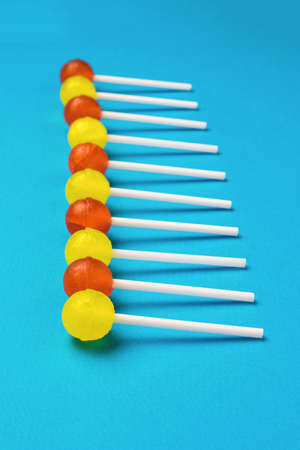 Yellow and red lollipops on a white background stacked in a row on a blue background. minimal...